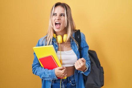 Téléchargez les photos : Jeune femme blonde portant un sac à dos étudiant et tenant des livres en colère et fous hurlant frustrés et furieux, criant de colère. rage et concept agressif. - en image libre de droit