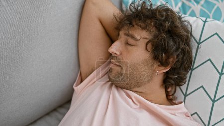 Photo for A young man with curly hair sleeps peacefully on a couch in a cozy home environment - Royalty Free Image