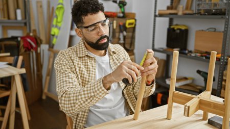 Foto de Un artesano barbudo mide piezas de madera con precisión en un estudio de carpintería bien equipado, mostrando habilidad y precisión. - Imagen libre de derechos