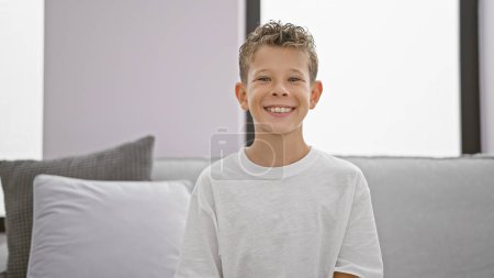 Photo for Adorable blond boy, full of confidence and joy, flashing a cheerful smile while relaxing comfortably on the sofa at home. - Royalty Free Image