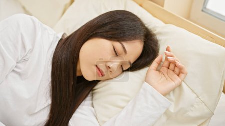 Téléchargez les photos : Une jeune femme asiatique sereine qui dort paisiblement dans une chambre lumineuse - en image libre de droit