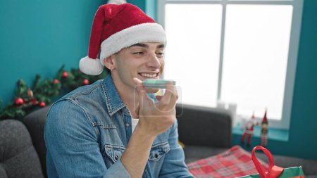 Téléchargez les photos : Jeune homme hispanique envoyant un message vocal par smartphone célébrant Noël à la maison - en image libre de droit