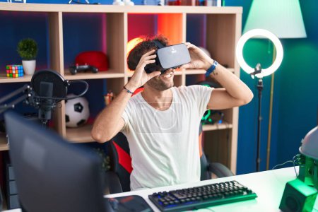Photo for Young hispanic man streamer playing video game using virtual reality glasses at music studio - Royalty Free Image