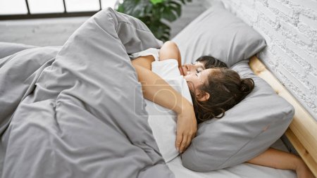 Téléchargez les photos : Allongés ensemble dans leur chambre confortable, une mère et sa fille partagent un câlin aimant avant de s'endormir sur le lit douillet de leur maison familiale. - en image libre de droit