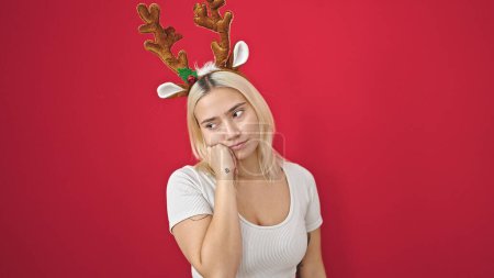 Téléchargez les photos : Jeune belle femme hispanique portant un chapeau de Noël en renne avec une expression de doute sur fond rouge isolé - en image libre de droit