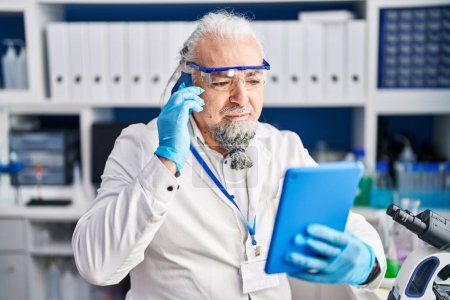 Téléchargez les photos : Middle age grey-haired man scientist talking on smartphone using touchpad at laboratory - en image libre de droit