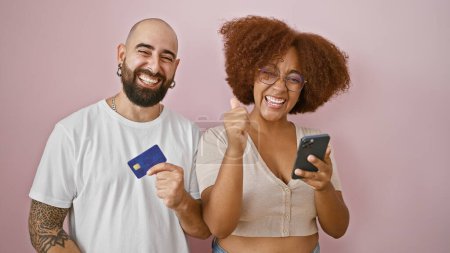 Foto de Hermosa pareja de pie juntos usando teléfono inteligente y tarjeta de crédito celebrando sobre fondo rosa aislado - Imagen libre de derechos