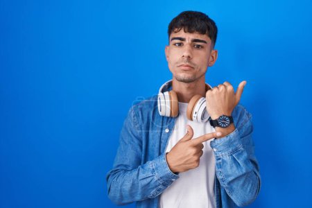 Téléchargez les photos : Jeune homme hispanique debout sur fond bleu pressé pointant vers regarder le temps, l'impatience, regardant la caméra avec une expression détendue - en image libre de droit