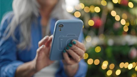 Foto de Mujer de pelo gris de mediana edad usando teléfono inteligente celebrando la Navidad en casa - Imagen libre de derechos
