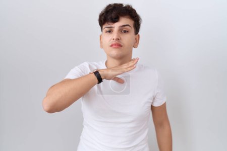 Téléchargez les photos : Jeune homme non binaire portant un t-shirt blanc décontracté tranchant la gorge avec la main comme couteau, menace d'agression avec une violence furieuse - en image libre de droit