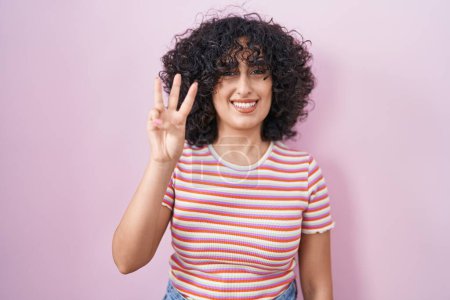 Photo for Young middle east woman standing over pink background showing and pointing up with fingers number three while smiling confident and happy. - Royalty Free Image