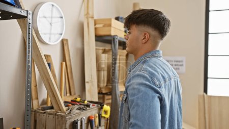 Photo for Handsome young hispanic man, a serious-faced professional carpenter, standing in his carpentry workshop amidst woodwork and timber - Royalty Free Image