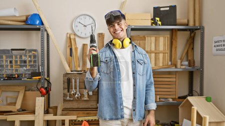 Photo for Young hispanic man carpenter wearing glasses and headphones holding drill at carpentry - Royalty Free Image