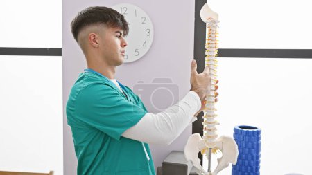 Photo for Handsome young hispanic man, a dedicated rehab therapist, gives eloquent speech while showcasing anatomical column model at bustling rehab clinic - Royalty Free Image