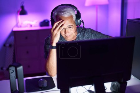 Foto de Edad media hombre de pelo gris streamer estresado utilizando ordenador en la sala de juegos - Imagen libre de derechos