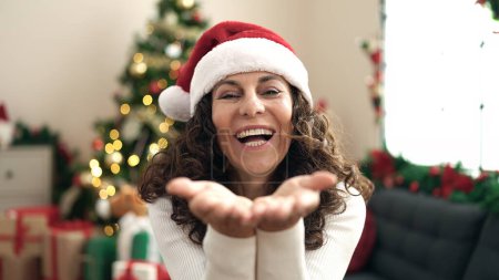 Photo for Middle age hispanic woman sitting on floor by christmas tree kissing at home - Royalty Free Image