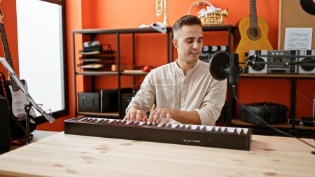 Foto de Un joven hispano toca el teclado en un estudio de música naranja lleno de instrumentos. - Imagen libre de derechos