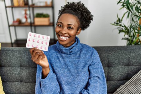 Photo for African american woman holding pills sitting on sofa at home - Royalty Free Image