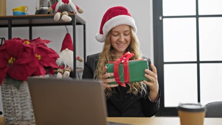 Téléchargez les photos : Jeune femme blonde ouvrière d'entreprise tenant cadeau de Noël travaillant au bureau - en image libre de droit