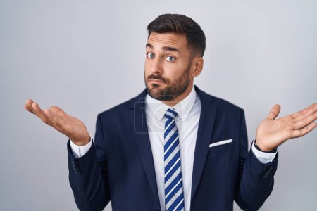 Photo for Handsome hispanic man wearing suit and tie clueless and confused expression with arms and hands raised. doubt concept. - Royalty Free Image