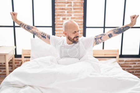 Photo for Young bald man waking up stretching arms at bedroom - Royalty Free Image
