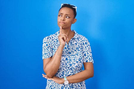 Photo for African american woman standing over blue background thinking concentrated about doubt with finger on chin and looking up wondering - Royalty Free Image