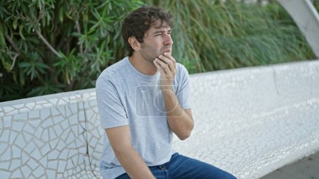 Photo for Young man sitting on bench looking to the side with serious expression at the park - Royalty Free Image