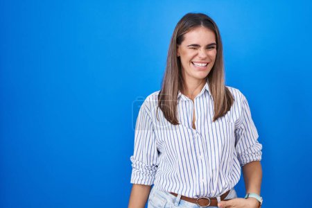 Téléchargez les photos : Hispanique jeune femme debout sur fond bleu clin d'oeil en regardant la caméra avec une expression sexy, gai et heureux visage. - en image libre de droit