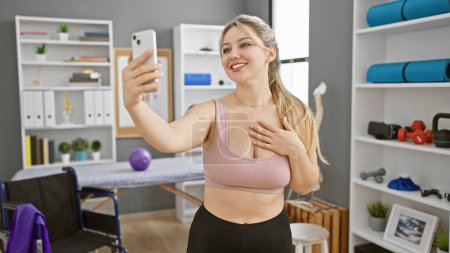 Photo for Blonde woman taking selfie in physical therapy clinic with fitness equipment - Royalty Free Image