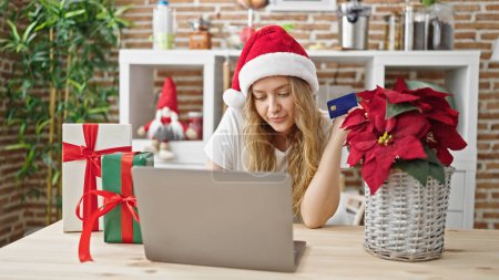 Foto de Joven rubia de compras con portátil y tarjeta de crédito celebrando la Navidad en el comedor - Imagen libre de derechos