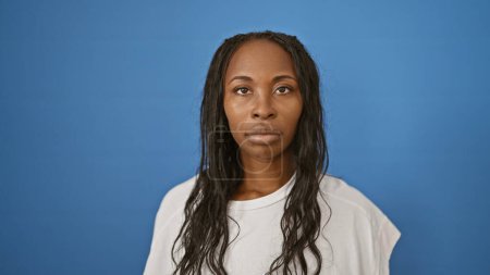 Photo for Serene african american woman with curly hair posing against a plain blue background for a contemporary portrait. - Royalty Free Image