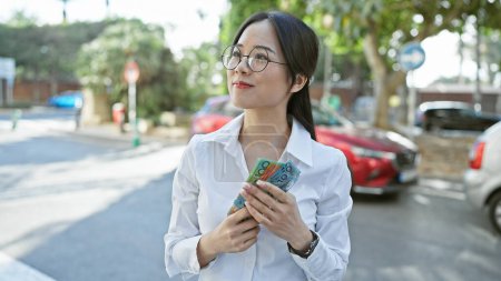 Photo for An asian woman counts australian dollars on an urban street, reflecting city life and financial themes. - Royalty Free Image