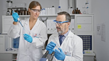 Photo for Two smiling scientists, mates in science, pouring liquid into a test tube using a pipette in an indoor lab, zoom in on their safety gloves while they discover new medical analysis together. - Royalty Free Image