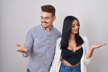 Téléchargez les photos : Jeune couple hispanique debout sur fond blanc souriant montrant les paumes ouvertes des deux mains, présentant et comparant la publicité et l'équilibre - en image libre de droit