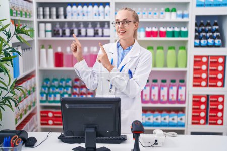 Photo for Young caucasian woman working at pharmacy drugstore smiling and looking at the camera pointing with two hands and fingers to the side. - Royalty Free Image