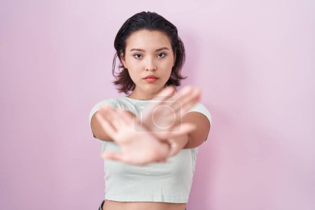 Photo for Hispanic young woman standing over pink background rejection expression crossing arms and palms doing negative sign, angry face - Royalty Free Image