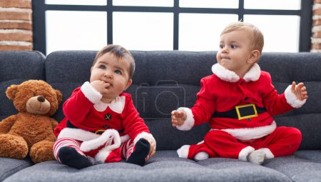 Foto de Adorable niño y niña con ropa de Navidad sentado en el sofá en casa - Imagen libre de derechos