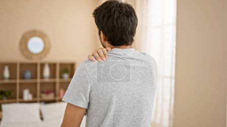 Téléchargez les photos : Rear view of a young man with a shoulder pain in a modern living room. - en image libre de droit