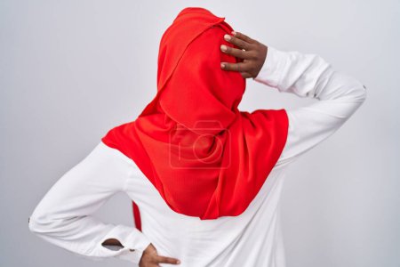 Téléchargez les photos : Jeune femme arabe portant l'écharpe traditionnelle islamique hijab vers l'arrière en pensant au doute avec la main sur la tête - en image libre de droit