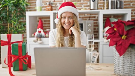 Photo for Young blonde woman celebrating christmas having video call drinking champagne at dinning room - Royalty Free Image