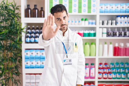 Photo for Handsome hispanic man working at pharmacy drugstore doing stop sing with palm of the hand. warning expression with negative and serious gesture on the face. - Royalty Free Image