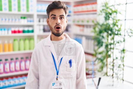 Photo for Young hispanic man with tattoos working at pharmacy drugstore scared and amazed with open mouth for surprise, disbelief face - Royalty Free Image