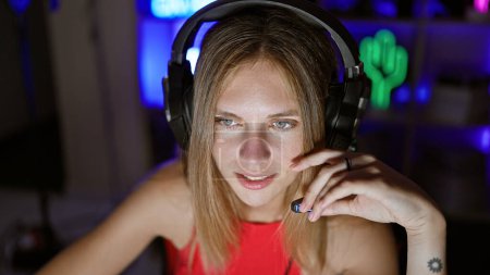Foto de Una joven atractiva mujer caucásica con el pelo rubio y los ojos azules con auriculares en una sala de juegos cubierta oscura - Imagen libre de derechos
