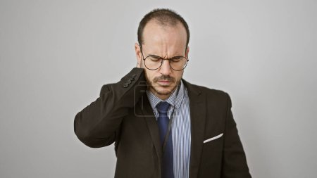 A hispanic man with a beard and glasses, wearing a suit, looks in pain against an isolated white background.