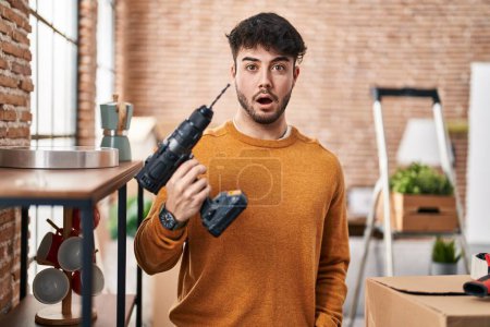 Photo for Hispanic man with beard holding screwdriver at new home scared and amazed with open mouth for surprise, disbelief face - Royalty Free Image