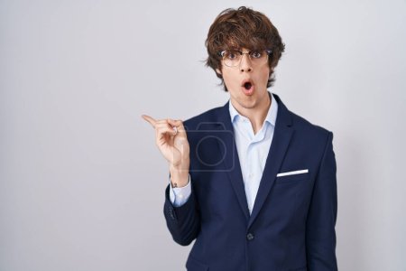 Photo for Hispanic business young man wearing glasses surprised pointing with finger to the side, open mouth amazed expression. - Royalty Free Image