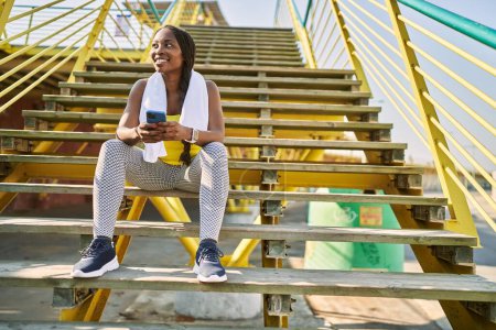 Téléchargez les photos : Femme afro-américaine en utilisant smartphone assis sur les escaliers à la rue - en image libre de droit