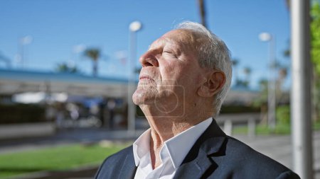 Photo for Balanced senior man enjoying meditating, calmly breathing in the city street with eyes closed, feeling the summer sunlight on his white hair - Royalty Free Image