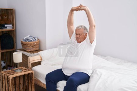 Téléchargez les photos : Middle age grey-haired man waking up stretching arms at bedroom - en image libre de droit