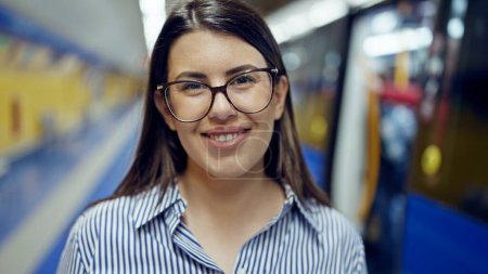 Foto de Joven mujer hispana hermosa sonriendo feliz esperando el metro en la estación de metro de Madrid - Imagen libre de derechos